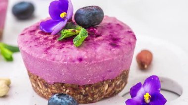 Blueberry and acai vegan cashew cakes with fresh berries, edible flowers, mint, nuts. Healthy vegan food concept. Tasty cheesecake. Close up.