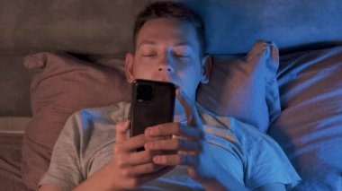 Akıllı telefonları kaydırırken, geceleri internette, sosyal medyada sörf yaparken karanlıkta sırt üstü uzanan bir adam. Akıllı telefon ve internet bağımlılığı. Uykusuzluk kavramı.