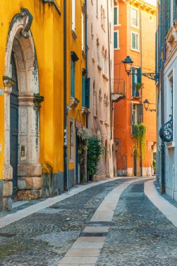 Gündoğumunda İtalya 'nın Veneto kentindeki Verona eski kasabasında renkli bina cepheleri ve kaldırımları olan ortaçağ dar sokakları. İtalyan caddesinde kimse yok. Dikey oryantasyon. Gidilecek yer