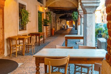 İtalya 'nın Veneto kentindeki Verona şehrinde tarihi kemer yollarının altında ahşap masaları ve sandalyeleri olan rahat bir kafeterya. Dar kaldırımda İtalyan tarzı kaldırım restoranı.