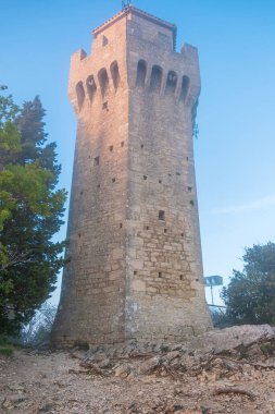 Montale Kulesi, San Marino 'nun üç kulesinin üçüncüsü, sisli günbatımında Monte Titano kayasına tünemişti. San Marino 'daki ortaçağ kalesi. Dikey oryantasyon. Seyahat ve turistik dönüm noktası