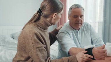 Genç bir kadın evde yaşlı bir adama kan basıncını ölçmesi için yardım ediyor. Kızı, yaşlı babasına tıbbi bir aletle kan basıncını ölçüyor. Bakım, sağlık denetimi ve aile desteği.
