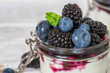 Böğürtlen ve böğürtlenli yoğurt parfe, granola ve böğürtlen sosunu cam kavanozda beyaz ahşap arka planda taze nane ile kapat. Taze böğürtlenli Yunan yoğurdu. Sağlıklı kahvaltı.. 