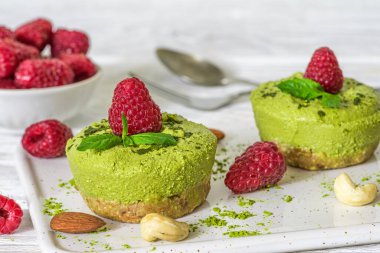 Ahududulu kirazlı vejetaryen peynirli kekler ve fındıklı beyaz tabakta nane şekeri ve yeşil çay tozu. Taze böğürtlenli çiğ vejetaryen kekleri. Sağlıklı vejetaryen tatlı. Kapat.