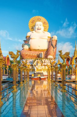 Koh Samui, Tayland 'daki Wat Plai Laem' de altın sütunlarla çevrili dev bir Buda heykeli ve tapınağa yansıyan döşeme yolu. Seyahat ve turistik dönüm noktası. Dikey