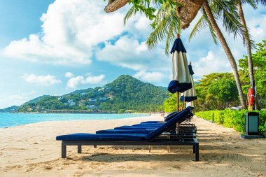 Plaj şezlongları ve şemsiyeler kumlu sahilde, tropikal dağ, turkuaz su okyanusu palmiye ağaçlarının altında güneşli bir günde. Tayland 'ın Koh Samui adasındaki Chaweng Noi kumlu plajı. Yaz tatili