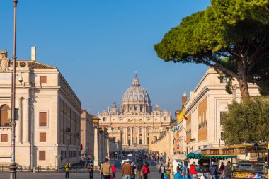 Vatikan, İtalya - 2 Mart 2024: Vatikan 'da Aziz Peters Bazilikası, güneşli bir günde Via della Conciliazione' den Piazza San Pietro 'ya giden kaldırım taşı caddesinde yürüyen turistlerle birlikte görülüyor. Seyahat