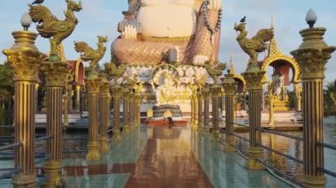 Koh Samui, Tayland 'daki Wat Plai Laem' de altın sütunlarla çevrili dev bir Buda heykeli ve tapınağa yansıyan döşeme yolu. Seyahat ve turistik dönüm noktası. 