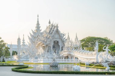 Beyaz Tapınak Wat Rong Khun, gün batımında yemyeşil bahçeyle çevrili su üzerinde köprüler, Chiang Rai, Tayland. Kuzey Tayland 'daki Budist tapınağı.