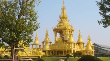 Wat Rong Khun kompleksindeki altın Ganesha tapınağı bahçeli ve güneşli bir günde mavi gökyüzü altında geleneksel mimari ile çevrili Chiang Rai, Tayland. Beyaz tapınak kompleksi.