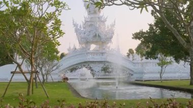 Beyaz tapınak kompleksindeki binalardan birine giden beyaz süslemeli köprü. Bahçesinde çeşme var, Chiang Rai, Tayland. Kuzey Tayland 'daki Budist Wat Rong Khun tapınağı. Seyahat simgesi.