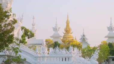 Gün batımında ağaçlar ve yeşilliklerle çevrili altın ve beyaz Budist tapınak yapıları, Chiang Rai, Tayland. Wat Rong Khun kompleksi. Asya 'da seyahat ve turistik dönüm noktası.