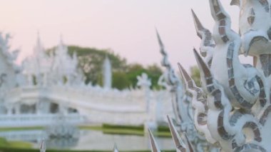 Beyaz tapınak Wat Rong Khun 'da gün batımında yemyeşil bahçeyle çevrili su birikintisi üzerindeki köprüler, Chiang Rai, Tayland. Kuzey Tayland 'daki Budist tapınağı.