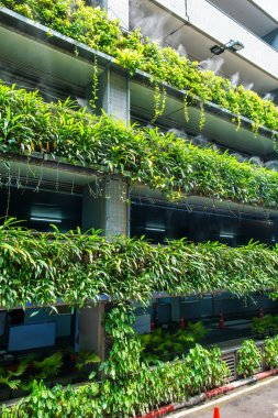 Otoparkın çok katlı ön cephesinde yeşil yapraklı dikey bahçe ve sisli sulama sürdürülebilir tasarımla Tayland 'ın Bangkok şehrindeki işlevsel kentsel mimarinin birleşimi. Kentsel soğutma