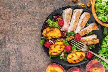 Şeftalili ızgara tavuk göğsü salatası, ahududu, ceviz ve kırsal ahşap arka planda çatalla siyah tabakta karışık yeşillikler. Kopyalama alanı olan üst görünüm. Sağlıklı diyet yemekleri. Yaz yemeği.