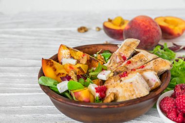 Şeftalili ızgara tavuk göğsü salatası, feta peyniri, ahududu, ceviz ve beyaz ahşap arka planda karışık yeşillikler. Kapatın. Sağlıklı diyet yemekleri. Yaz yemeği..