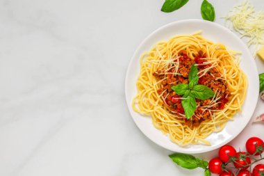 Sığır eti soslu spagetti bolonez ve mermer arka planda taze fesleğenle beyaz tabakta rendelenmiş parmesan peyniri. Kopyalama alanı olan üst görünüm. İtalyan yemeği. Lezzetli yemek..