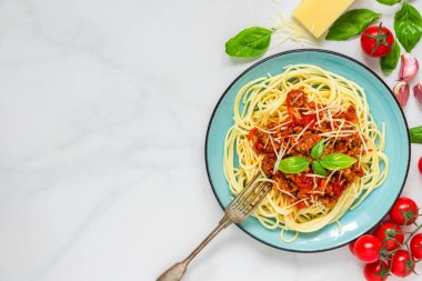 Sığır eti soslu spagetti bolonez, fesleğen ve rendelenmiş parmesan peyniri mavi tabakta beyaz mermer arka planda çatalla. Kopyalama alanı olan üst görünüm. İtalyan makarnası. Lezzetli yemek..