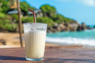 Samui Adası, Tayland 'daki sahil kafeteryasında, ahşap bir masa üzerinde, cam içinde hindistan cevizli smoothie tazeliyorum. Coral Cove sahilindeki yaz restoranında soğuk tropikal milkshake..