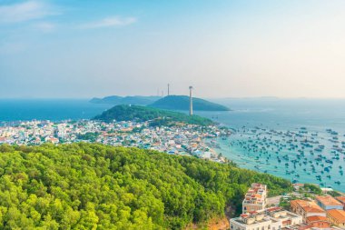 Yoğun yeşil ormanı olan kıyı kasabasının havadan görünüşü, mavi denizde balıkçı tekneleri ve Phu Quoc Adası, Vietnam 'daki adalar arasında uzanan teleferik. Modern Hon Thom teleferik sistemi. Turizm