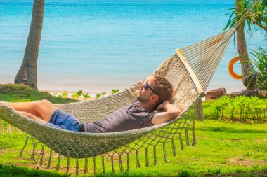 Turkuaz denizli hamakta dinlenen erkek turist güneşli bir günde palmiye ağaçları altında huzurlu bir yaz tatili geçiriyor. Kaygısız ve huzurlu bir tatil anı. Phu Quoc Adası.