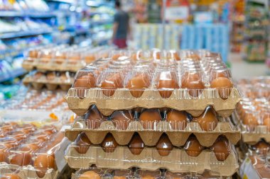 Kartonda kahverengi yumurtalar ve süpermarket koridorunda sergilenen plastik tepsiler. Market alışverişi, taze gıda tedariği, perakende satış ve gıda ambalajı. Tayland 'da bakkal.