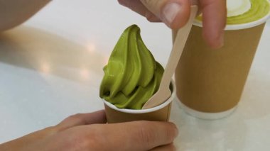 Beyaz masada kağıt bardak matcha latte 'nin yanında tahta kaşıkla kibritli dondurma yiyen adam el ele tutuşuyor. Sıcak içecek ve çevre dostu yemeklerde Japon yeşil çay tatlısı. Sürdürülebilir