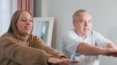 Yetişkin kız, yaşlı babasına evde kollarını açarak yavaş denge egzersizleri yapmayı öğretiyor. Evde sağlık, aile desteği, kıdemli fitness, nesiller arası bağ, sağlıklı.