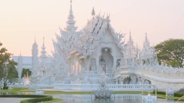 Beyaz tapınak Wat Rong Khun çevresi yemyeşil bahçe ve gün batımında gölet ile çevrili, Chiang Rai, Tayland. Kuzey Tayland 'daki Budist tapınağı. Asya 'da seyahat ve turistik dönüm noktası.