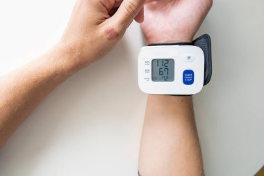 Kan basıncı ve nabzı ölçmek için dijital bilek basıncı monitörü kullanan bir adam. Hipertansiyon, kalp sağlığı ve genel sağlık kontrolü. Düzenli sağlık izleme teknolojisi. Kişisel bakım ve...