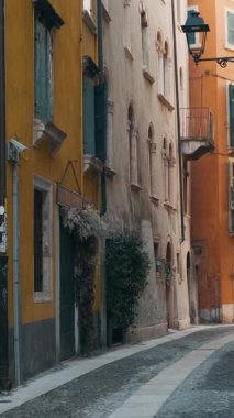 Gündoğumunda İtalya 'nın Veneto kentindeki Verona eski kasabasında renkli bina cepheleri ve kaldırımları olan ortaçağ dar sokakları. İtalyan caddesinde kimse yok. Dikey oryantasyon. Gidilecek yer