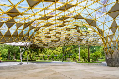 Sarı geometrik çatılı modern mimari yapı ve Perdana Botanik Bahçesi, Kuala Lumpur, Malezya, Asya 'da yeşillik ve ağaçlarla çevrili geniş açık alan.