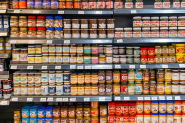 Kuala Lumpur, Malezya - Haziran 06 2024: Fıstık ezmesi, fındık ezmesi ve reçel markalarıyla dolu süpermarket rafları. arka arkaya. Yiyecek reyonu olan bir bakkal. Perakende işi.