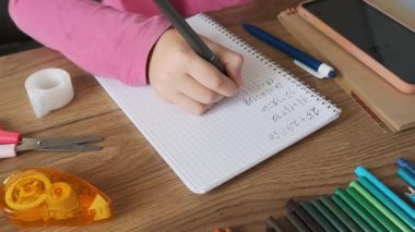 Çocuk, ahşap masadaki kırtasiyeyle defterde matematik alıştırmaları yapıyor. Okul ödevi olarak kız el yazısı matematik denklemleri. Okula dönüş, öğrenme, eğitim kavramı.