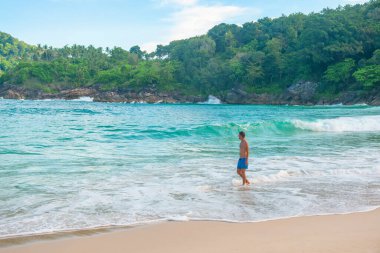 Tayland 'ın Phuket adasında, turkuaz dalgalar ve yemyeşil ormanlarla tropik sahil kıyılarında yürüyen bir adam. Özgürlük plajında yalnız erkek turist. Popüler yaz ve kış tatilleri
