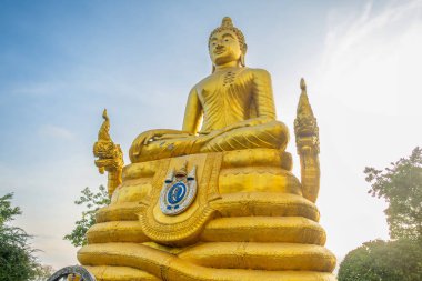 Altın Buda heykeli, Tayland 'daki Phuket Adası' ndaki Büyük Buda Tapınağı 'nda gün batımında dekoratif temeller ve açık gökyüzü altında naga ayrıntıları ile meditasyonda poz veriyor. Tayland 'da Budizm, kutsal mimari