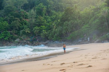 Adam, Tayland 'ın Phuket Adası' ndaki turkuaz dalgalar ve yemyeşil ormanlarla tropik sahillerdeki sığ dalgalarda tek başına sörf yapıyor. Özgürlük plajında yalnız erkek turist. Popüler yaz tatili