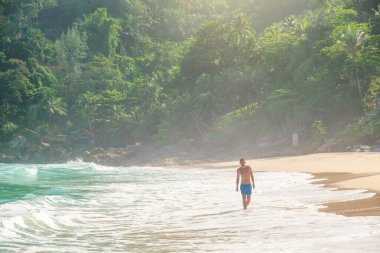 Tayland 'ın Phuket adasında, turkuaz dalgalar ve yemyeşil ormanlarla tropik sahil kıyılarında yürüyen bir adam. Özgürlük plajında yalnız erkek turist. Popüler yaz ve kış tatilleri