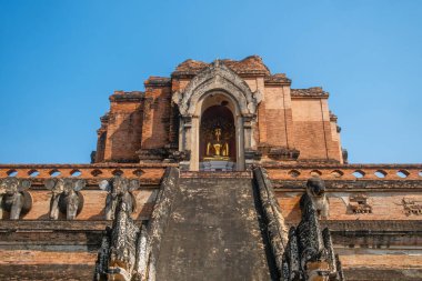 Ancient brick stupa of Wat Chedi Luang temple with golden Buddha statue seated in alcove under clear blue sky in Chiang Mai, Thailand. Buddhist temple. Thai religious architecture. Travel and