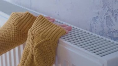 Soğuk kış günlerinde evdeki ısıtıcının üstünde ellerini sarı kazakla ısıtan bir adam. Erkek, kaloriferin üzerinde ısınıyor. Isınma mevsimi ya da soğuk hava kavramı.