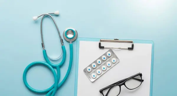 A stethoscope, pills, glasses, and clipboard on a blue background. Perfect for healthcare, medicine, and medical-related content. Professional and clean design.