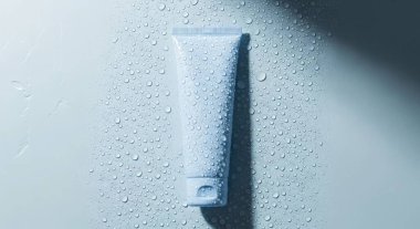 A pristine white cosmetic tube, adorned with water drops, rests against a clean white backdrop. Perfect for showcasing skincare or beauty product mockups with elegance.