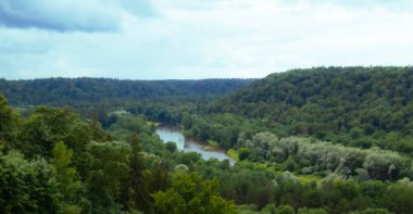 Nehir vadisi bulutlu yeşil ağaçlarla çevrili.