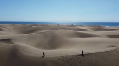 Drone captures two hikers on Maspalomas dunes in Gran Canaria with stunning Atlantic Ocean on horizon
