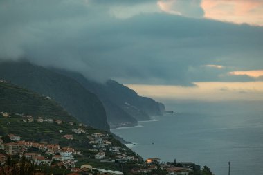 Denize uzanan ve sis dolu bulutlarla çevrili görkemli dağlarıyla kıyı şehrinin hayranlık uyandıran manzarası. Madeira, İspanya