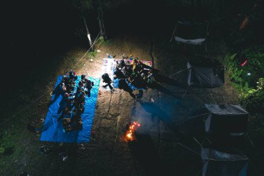 Ormanın ortasında kamp ateşi yakarken öğrenci kampı aktivitelerinin havadan görüntüsü.