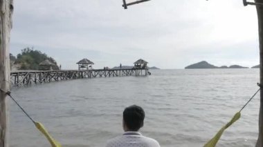 Pesisir Selatan - 2 Haziran 2019: Manjuto sahilinde salıncakta oturan adam. Batı Sumatra 'nın pesisir selatan bölgesinde Manjuto plaj turizminin güzelliğinin hava manzarasını oluşturun. d-log ham stok videosu