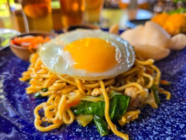 Yumurta ve sebzelerle dolu kızarmış şehriye. Ahşap bir masada servis ediliyor. Endonezya usulü hazır erişte.