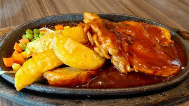 Kızarmış patates kızartması ve siyah ahşap tabakta sebzeli kızarmış tavuk bifteği.