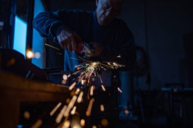 İşçi, emekli, atölyesinde öğütücüyle metal öğütüyor. Kameraya doğru kıvılcımlar saçıyor..